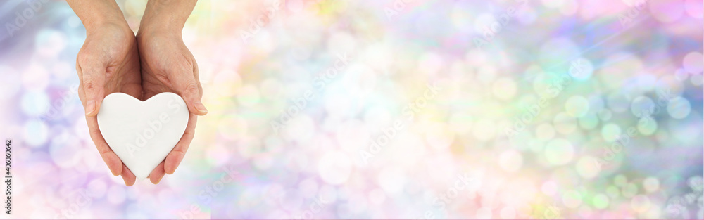 Sending messages of love and kindness bokeh banner - female hands holding a white heart plaque against a wide rainbow coloured bokeh background with copy space for messages Sending messages of love and kindness bokeh banner - female hands holding a white heart plaque against a wide rainbow coloured bokeh background with copy space for messages