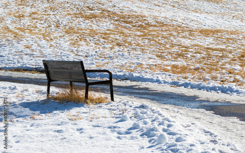empty black metal bench near a snow covered hillside on a sunny day with copy space