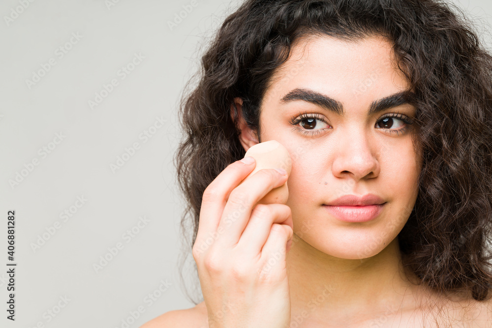 Young woman putting on makeup for even skin