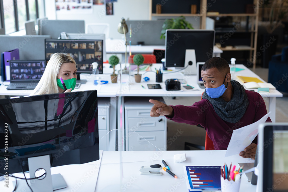Two diverse business people wearing face masks in creative office - obrazy, fototapety, plakaty 