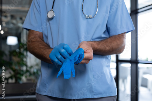Caucasian male doctor standing putting protective gloves on