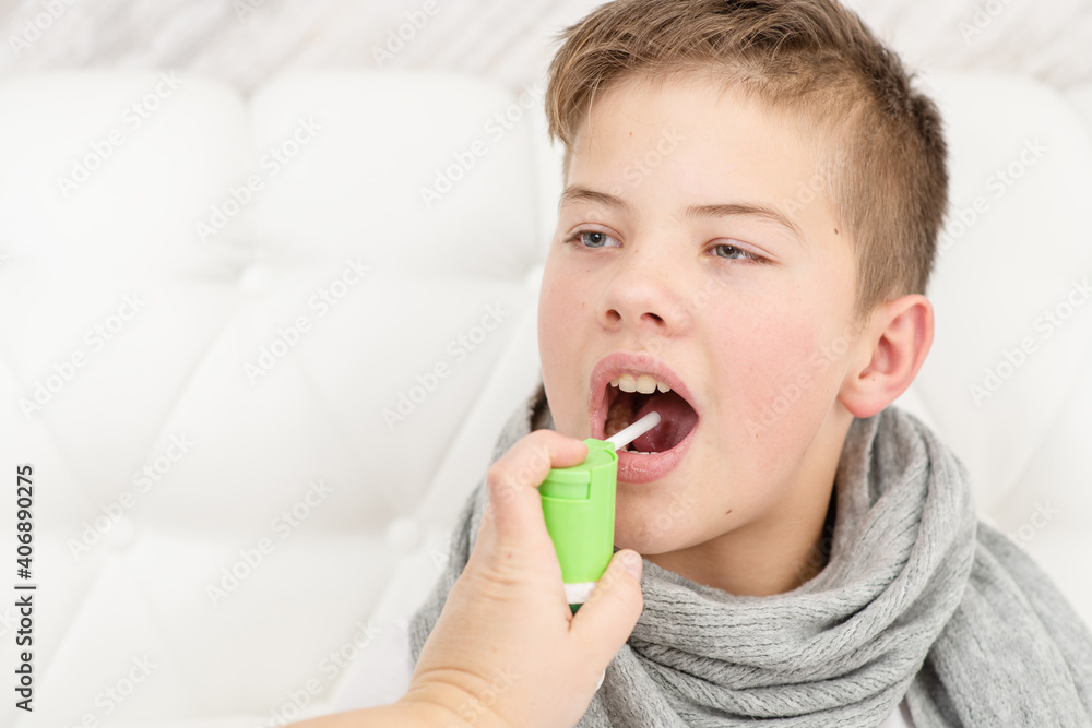 A sick child lies on the bed in a warm scarf and sprinkles medicine down his throat. Cold treatment concept A sick child lies on the bed in a warm scarf and sprinkles medicine down his throat. Cold treatment concept
