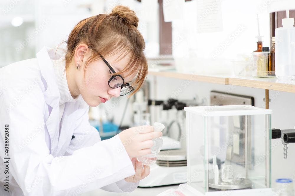 In a chemical laboratory, a girl laboratory assistant weighs a chemical in powder on a special scale. Assistant in the chemistry laboratory at the university In a chemical laboratory, a girl laboratory assistant weighs a chemical in powder on a special scale. Assistant in the chemistry laboratory at the university