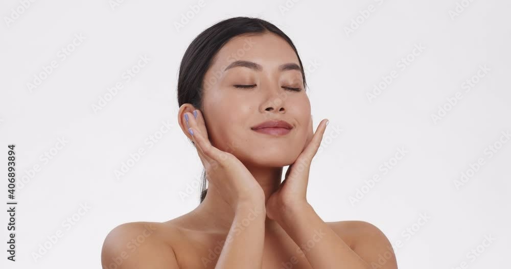 Young asian lady caressing her face skin, enjoying perfect body condition, white studio background, slow motion Young asian lady caressing her face skin, enjoying perfect body condition, white studio background, slow motion