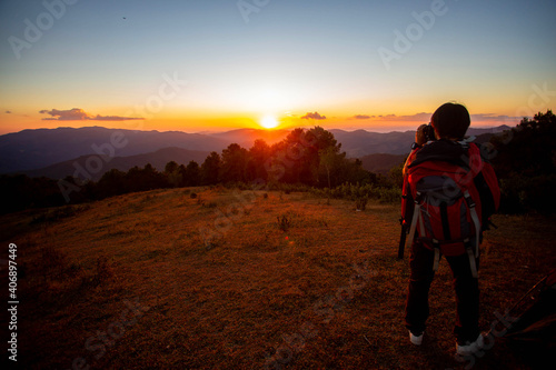 A man who loves adventure and photography. Stand on the top of the mountain with a tent, enjoy the beautiful view at sunset.