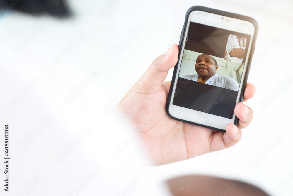 Woman's hand uses a smartphone online video call consultation app to an African male doctor for assistance for remote patients, videoconferencing on smartphone , telemedicine