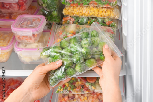 Woman putting plastic bag with frozen vegetables into refrigerator