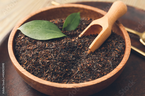 Obraz na płótnie Bowl with dry black tea leaves and scoop on wooden background