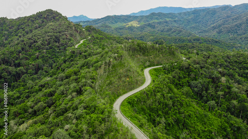 Top view of countryside road passing through the green forest and mountain in Thailand.