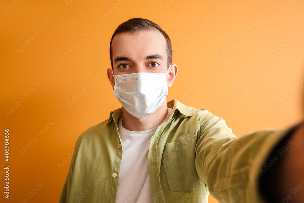 Young man in medical mask taking selfie on color background Young man in medical mask taking selfie on color background