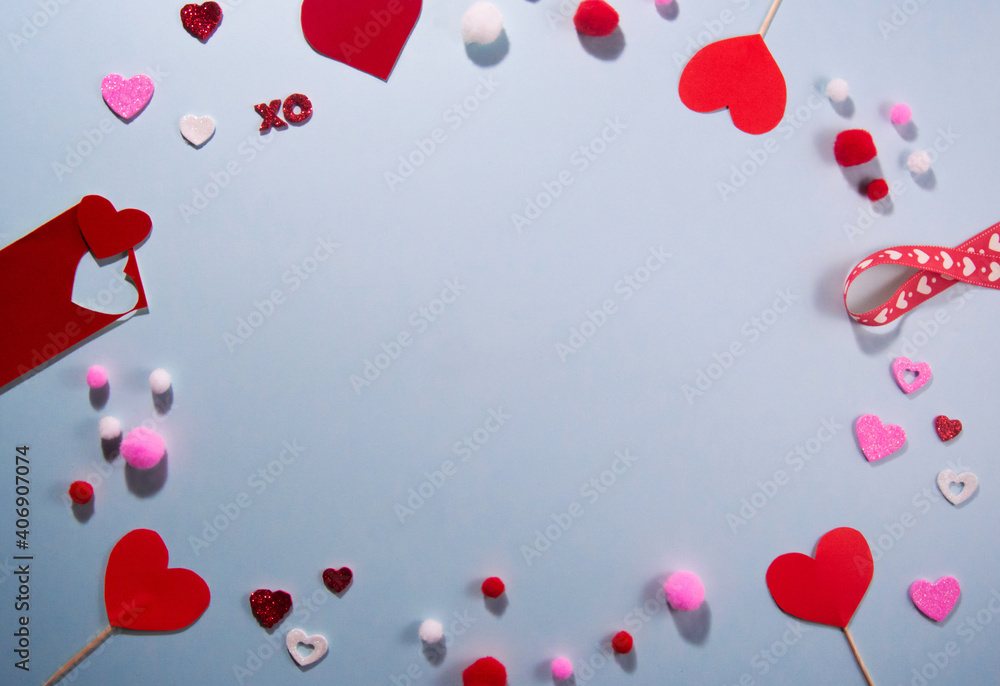 Frame of decorations for design for valentine's day on a blue background. White and red paper hearts, ribbon with hearts, pom-poms, paper cut hearts. Flat lay top view. Copy space