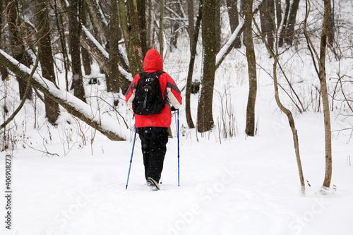 Nordic walking, healthy lifestyle. Man with backpack and sticks in winter park during snowfall, adventure and travel in cold weather 