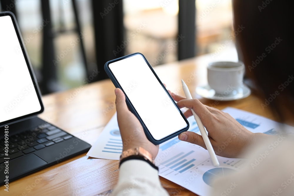 Close up view of businesswoman using smart phone and analyzing marketing research charts on paper document at office. Close up view of businesswoman using smart phone and analyzing marketing research charts on paper document at office.