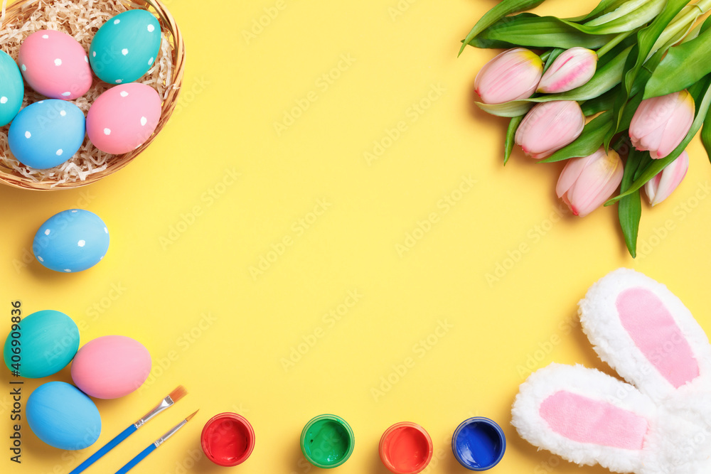 Happy easter. Multi-colored eggs in a basket, rabbit ears, tulips and paints on a yellow background. Flat lay greeting card. Copy space on medical protective mask. Happy easter. Multi-colored eggs in a basket, rabbit ears, tulips and paints on a yellow background. Flat lay greeting card. Copy space on medical protective mask.