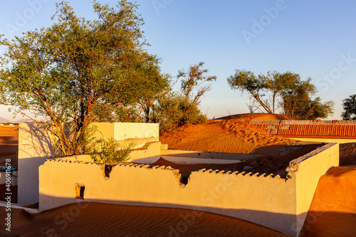 Al Madam ghost town buildings and walls buried in sand dunes in the desert of Sharjah, United Arab Emirates, sunset.