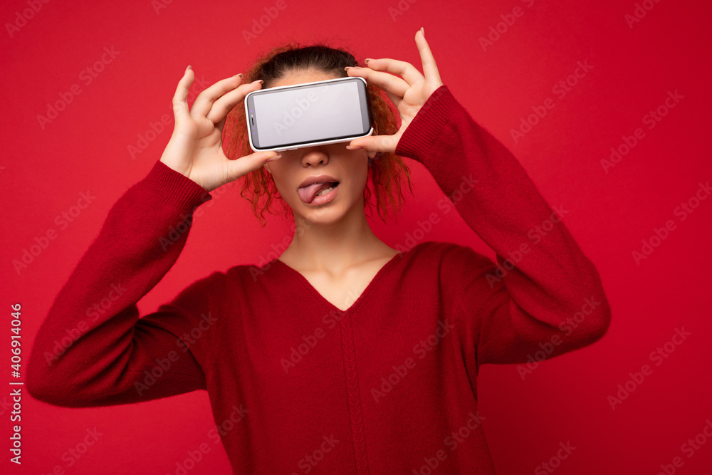Photo portrait of happy funny young woman wearing dark red sweater isolated over red background holding smartphone and showing mobile phone screen with empty space for mockup having fun and showing Photo portrait of happy funny young woman wearing dark red sweater isolated over red background holding smartphone and showing mobile phone screen with empty space for mockup having fun and showing
