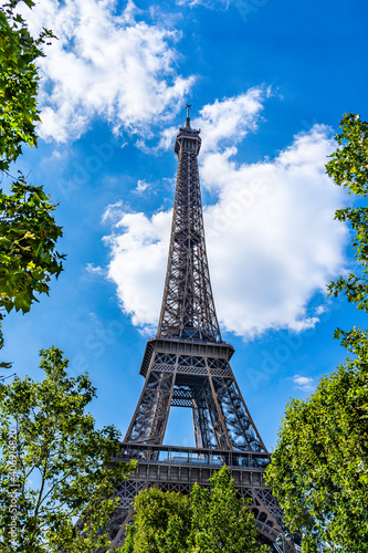 Fototapeta Naklejka Na Ścianę i Meble -  The Eiffel Tower surrounded by green tree leaves in Paris, France on a blue sky with white clouds background