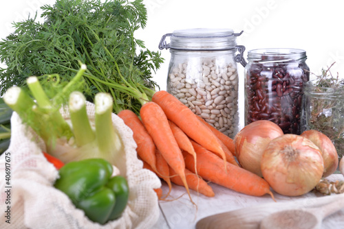 fresh vegetables and dry beans in jar with onions and garlic on a table on wh...