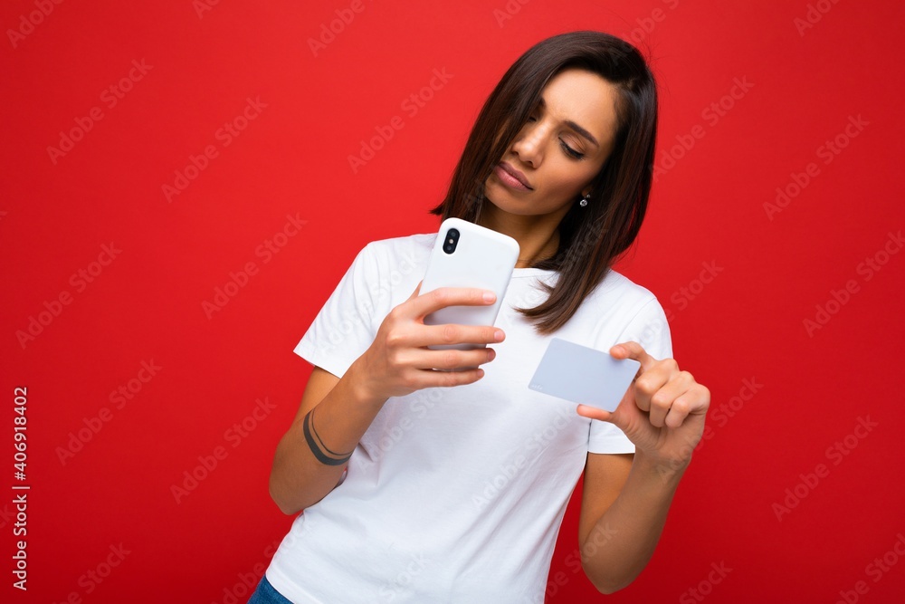 Pretty woman wearing everyday stylish clothes isolated on background wall holding and using phone and credit card making payment looking at smartphone screen Pretty woman wearing everyday stylish clothes isolated on background wall holding and using phone and credit card making payment looking at smartphone screen
