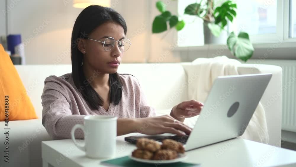 African woman with laptop at table works online at home Spbd. Female black model had glasses and beauty blouse. In background is home setting with plant and window. In room beautiful ethnic person African woman with laptop at table works online at home Spbd. Female black model had glasses and beauty blouse. In background is home setting with plant and window. In room beautiful ethnic person