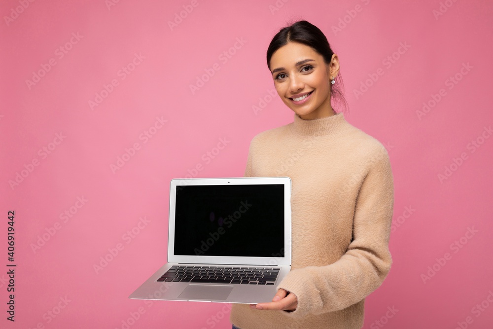 Photo of beautiful young woman holding computer laptop looking at camera isolated over colourful background Photo of beautiful young woman holding computer laptop looking at camera isolated over colourful background