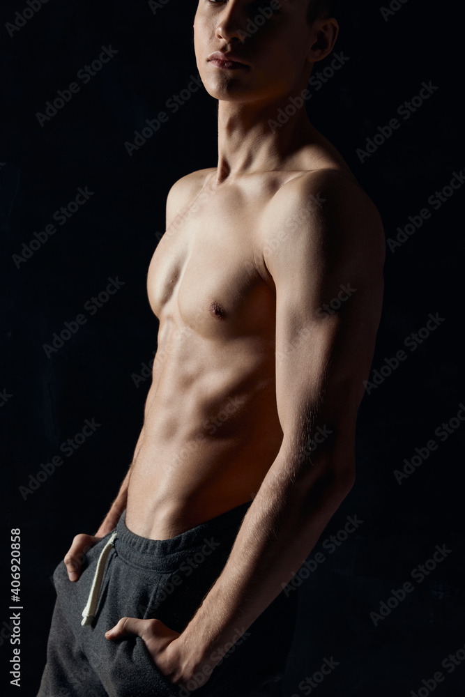 Fototapeta premium athlete with a pumped-up torso holds his hands in his pants pockets on a black background