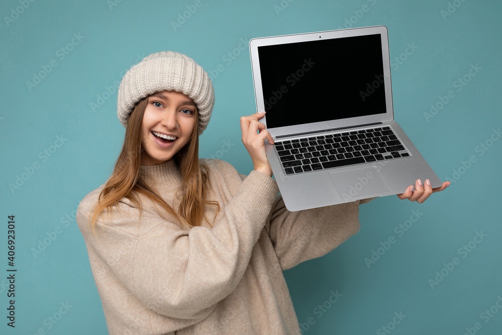 beautiful charming fascinating pretty smiling happy young dark blond feemale student woman in winter warm knitted beige hat holding computer laptop looking at camera wearing beige winter sweater beautiful charming fascinating pretty smiling happy young dark blond feemale student woman in winter warm knitted beige hat holding computer laptop looking at camera wearing beige winter sweater