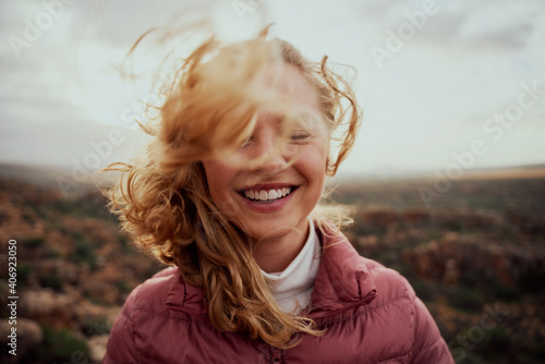 Portrait of young smiling woman face partially covered with flying hair in windy day standing at mountain - carefree woman photo