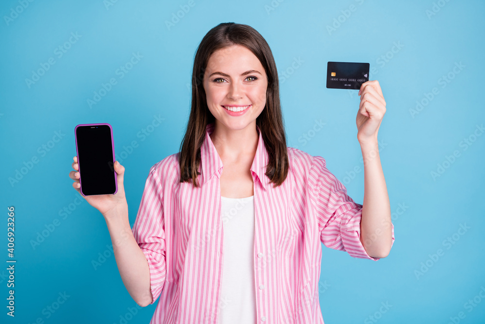 Photo portrait of smiling woman holding phone with blank space credit card in hands isolated on pastel blue colored background Photo portrait of smiling woman holding phone with blank space credit card in hands isolated on pastel blue colored background