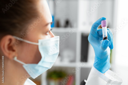 Female laboratory worker in mask holding test tube with blood sample