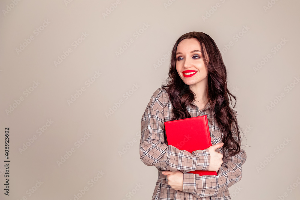 a beautiful young girl with red lips holds a red notebook in her hands. student. businesswoman on isolated gray background a beautiful young girl with red lips holds a red notebook in her hands. student. businesswoman on isolated gray background