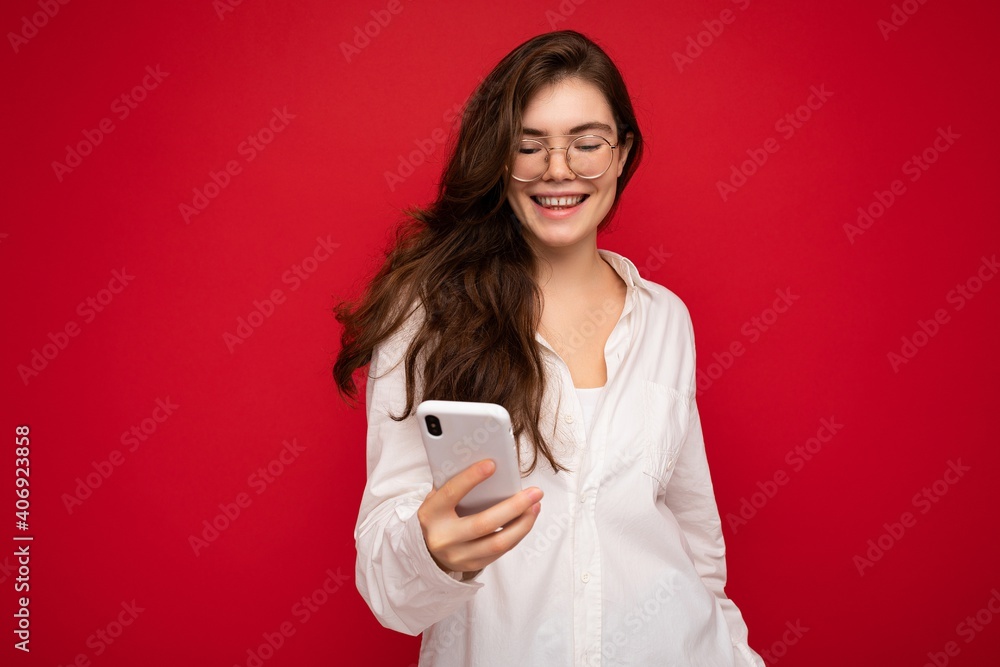 Photo shot of attractive positive good looking young woman wearing casual stylish outfit poising isolated on background with empty space holding in hand and using mobile phone messaging sms looking at Photo shot of attractive positive good looking young woman wearing casual stylish outfit poising isolated on background with empty space holding in hand and using mobile phone messaging sms looking at