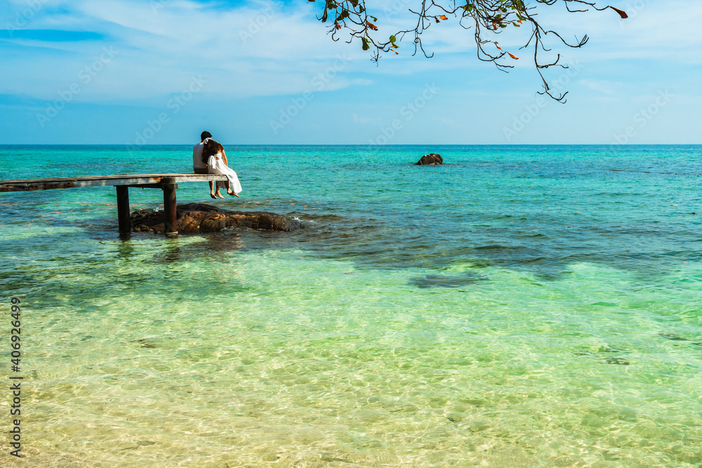 Obraz premium happy young couple sitting on wood bridge and sea beach at Koh MunNork Island, Rayong, Thailand