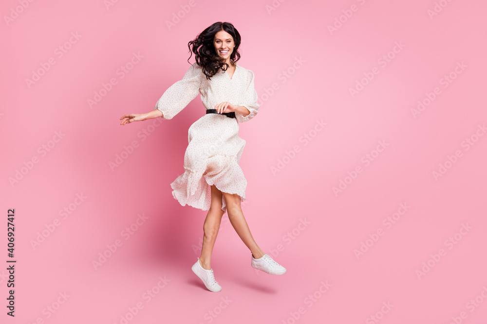 Full length body size photo of cheerful happy girl jumping up in dotted dress smiling dancing isolated pastel pink color background Full length body size photo of cheerful happy girl jumping up in dotted dress smiling dancing isolated pastel pink color background