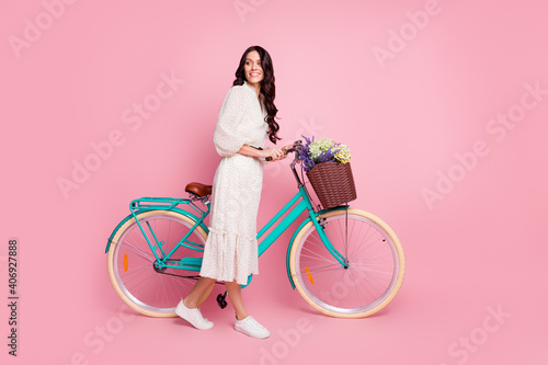 Fototapeta Naklejka Na Ścianę i Meble -  Full length body size photo of curious girl keeping bike with wild flowers looking blank space isolated on pastel pink color background