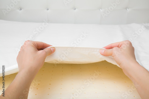 Young adult woman hands opening white cover and looking at yellow rubber foam inside orthopedic mattress. Closeup. Point of view shot.