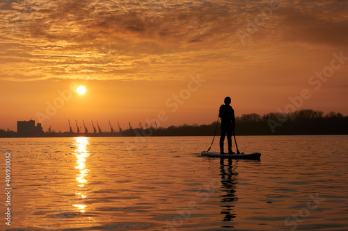 Silhouette of a boy standing on SUP during a beautiful winter sunrise on the river