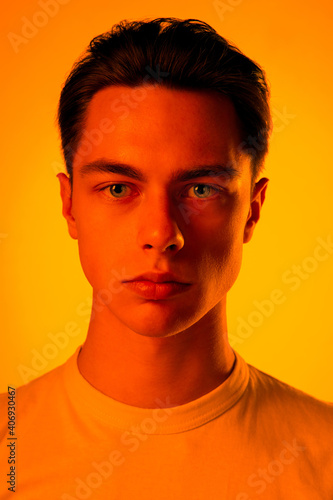 Warm. Handsome caucasian man's portrait isolated on orange studio background in neon, monochrome. Beautiful male model. Concept of human emotions, facial expression, sales, ad, fashion and beauty.