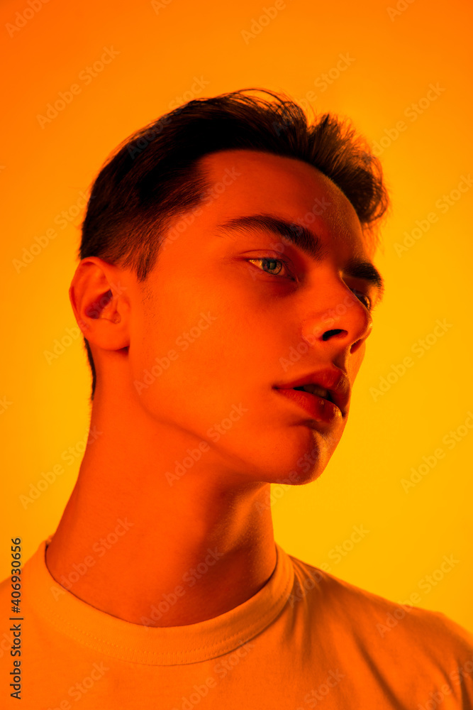 Warm. Handsome caucasian man's portrait isolated on orange studio background in neon, monochrome. Beautiful male model. Concept of human emotions, facial expression, sales, ad, fashion and beauty. Warm. Handsome caucasian man's portrait isolated on orange studio background in neon, monochrome. Beautiful male model. Concept of human emotions, facial expression, sales, ad, fashion and beauty.