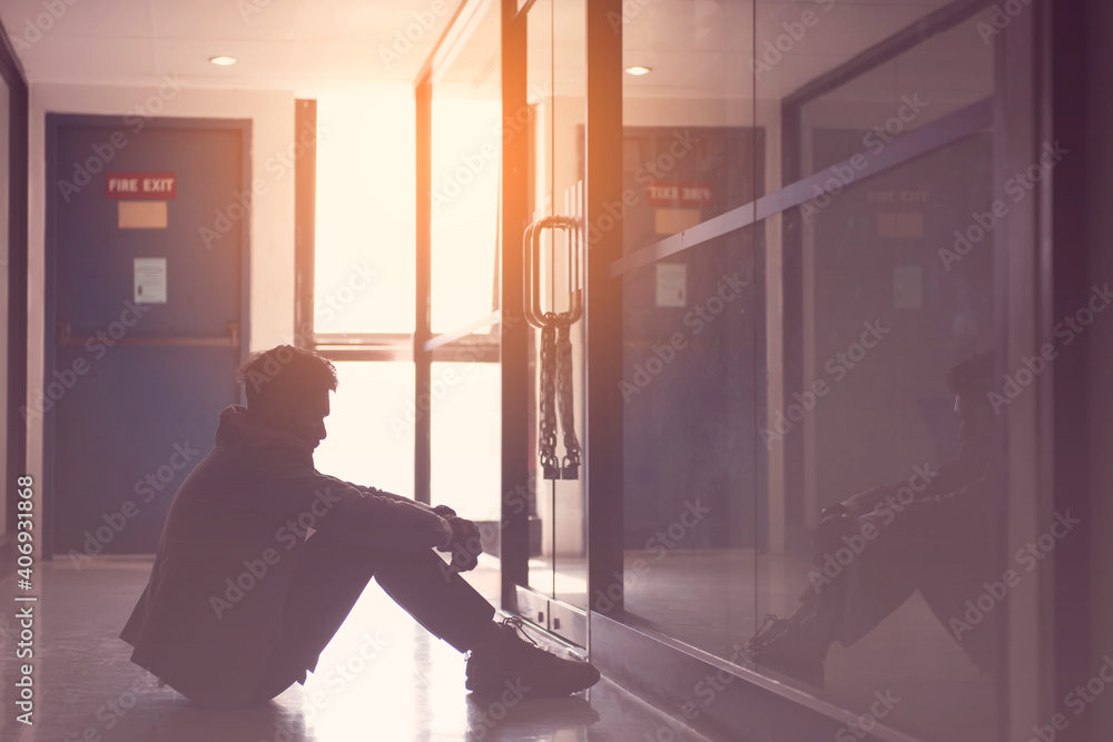 Silhouette of Serious Man sitting hug his knee alone infront of closeing office.With his reflecing shodow.