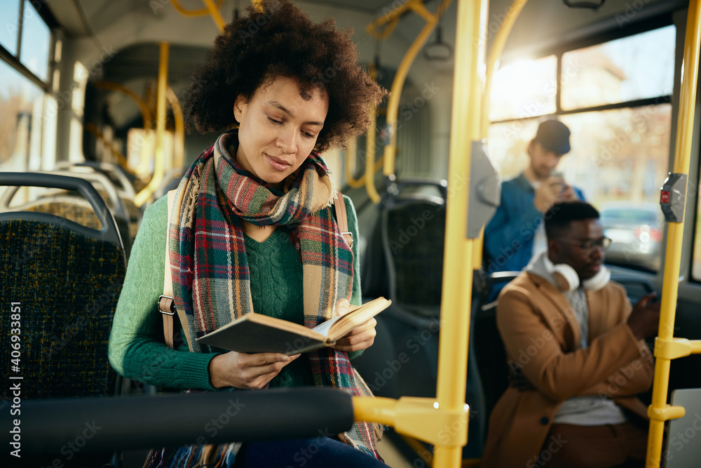 African American woman reading book wile commuting by bus.