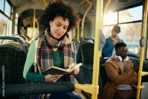 African American woman reading book wile commuting by bus.