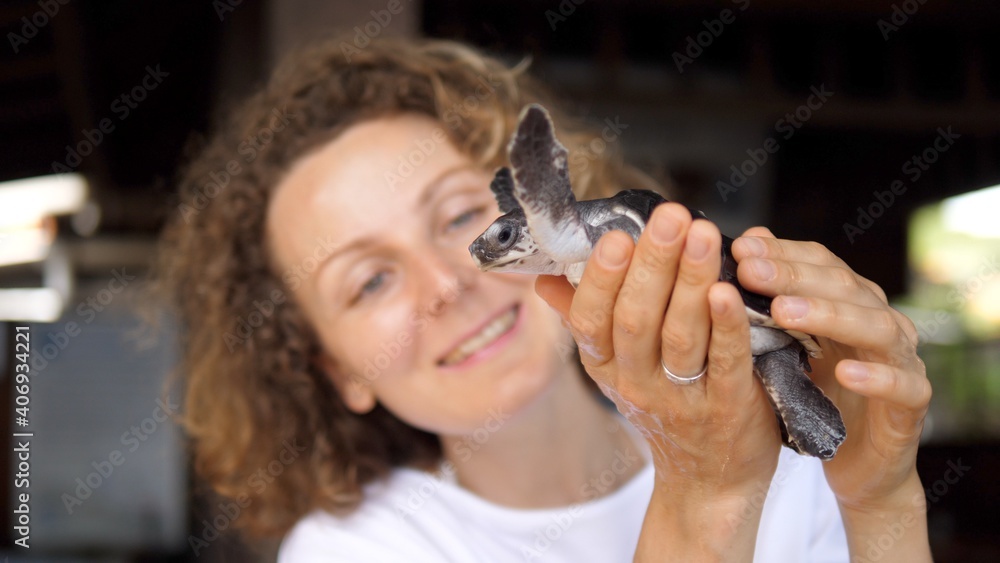Happy Caucasian young woman holding a turtle in her hands and looking at it with grate joy and happiness