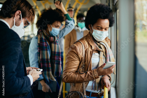 Black woman with face mask text messaging on cell phone while commuting by bus.