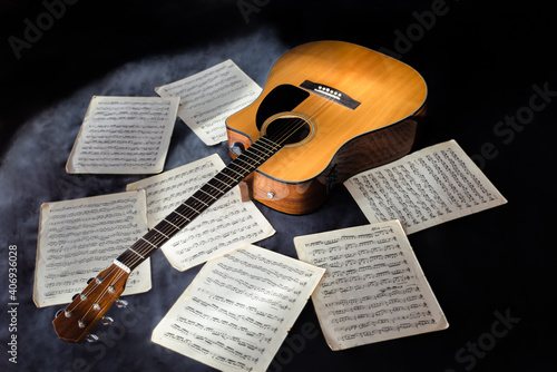 classic yellow color acoustic six-string guitar and sheet music letters with notes on isolated black background surrounded by fog