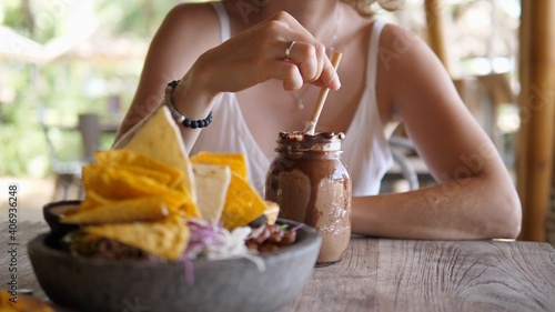 Beautiful young blonde woman enjoys her chocolate milkshake while having lunch alone at a beach restaurant. Solo travel