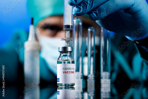 Medico con protezioni mediche e guanti in lattice preleva del il  vaccino anti-covid con una siringa  in un tavolo con diverse fialette  photo
