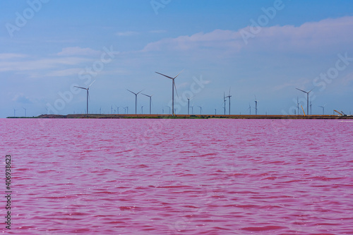 Wind turbines at the shore of lake with pink water. Clean energy. Ecological concept