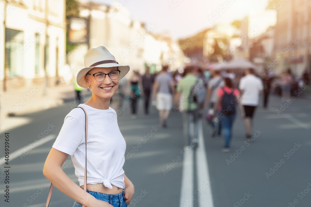 Young adult beautiful stylish single skinhead woman in white t-short, hat and jeans enjoy walking shopping city street on warm summer sunny day. Happy female person urban outdoors. Hipster lifestyle