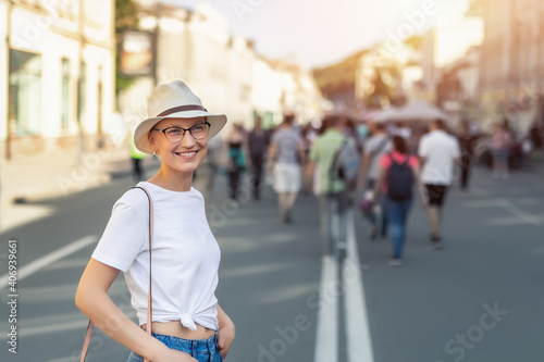 Fotografija Young adult beautiful stylish single skinhead woman in white t-short, hat and jeans enjoy walking shopping city street on warm summer sunny day
